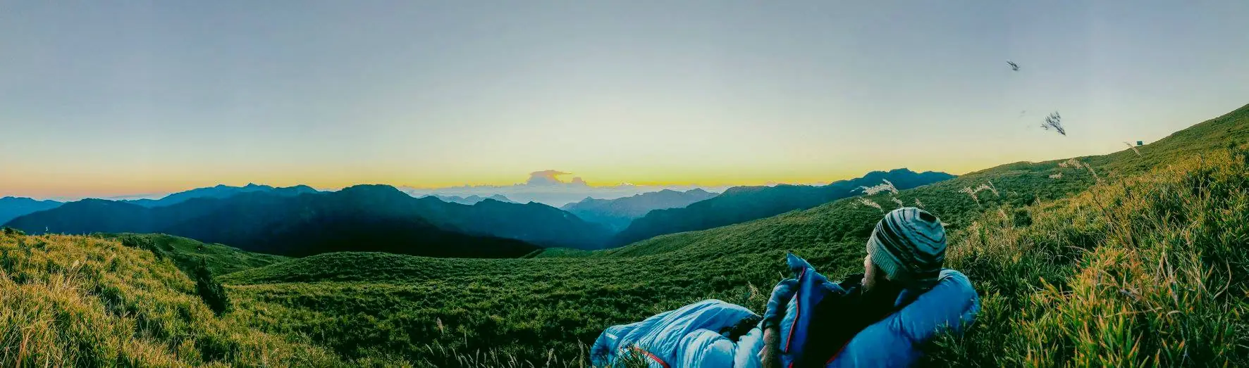 夕暮的高山草原，一個人躺在草坡上看著遠方的山稜